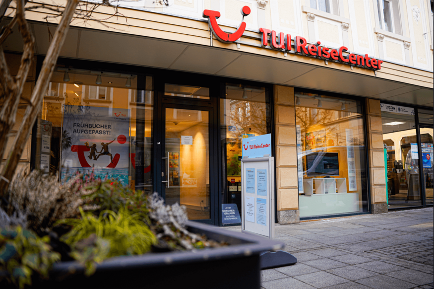 Außenansicht eines TUI ReiseCenters mit beleuchtetem Schaufenster in der Dämmerung.